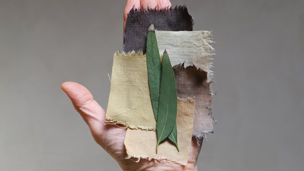 earth toned swatches of linen dyes with eucalyptus in hand with leaves on top